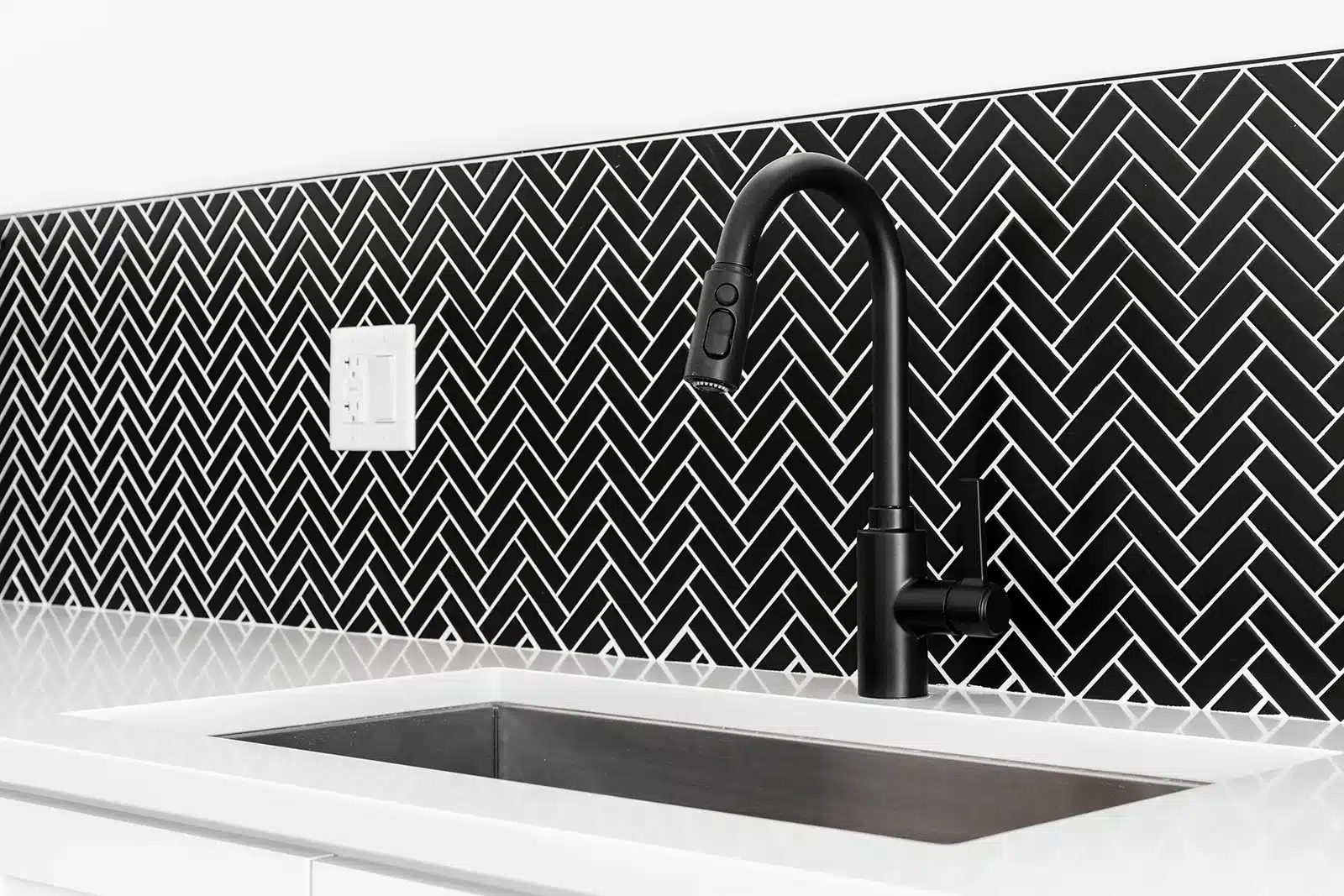 Modern kitchen with a striking black and white geometric backsplash and a matte black faucet, featuring conveniently placed electrical outlets.