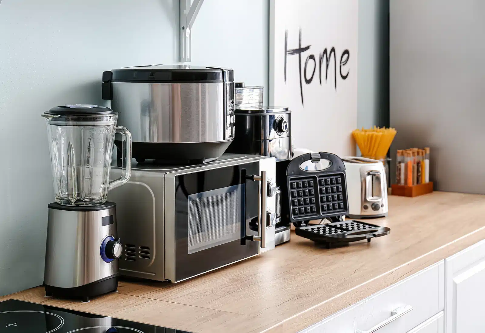 Modern kitchen countertop displaying an array of contemporary appliances including a blender, multi-cooker, coffee maker, and waffle iron, showcasing modern technology in the home.