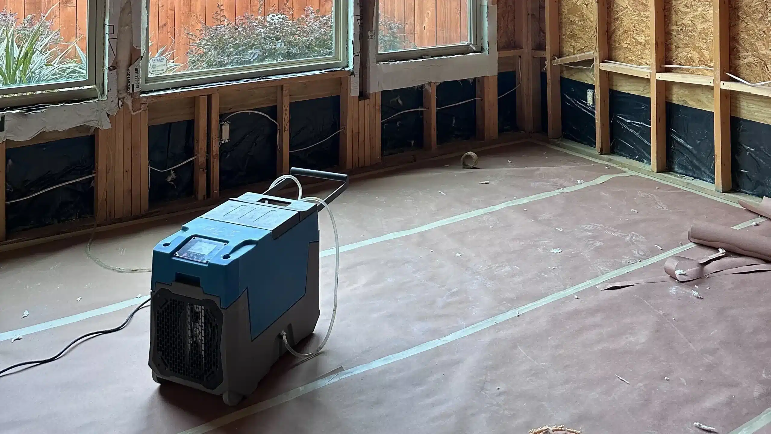 A dehumidifier operating in a room stripped down for water damage restoration, with exposed insulation.