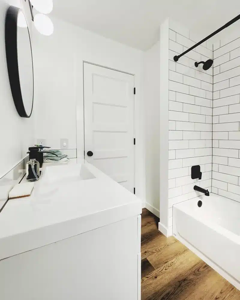 A sleek white bathroom corner with a countertop sink and a view towards a subway-tiled bathtub.