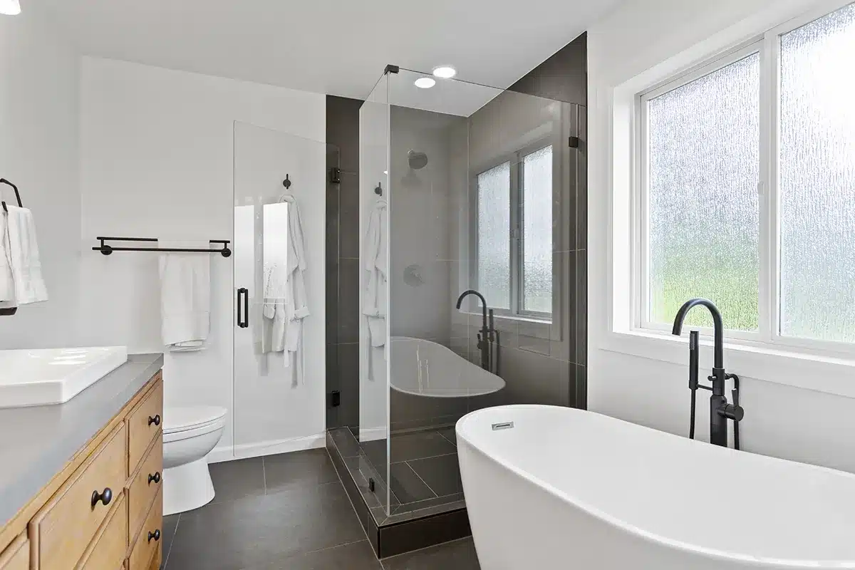 Seamlessly blending functionality and style, this Puyallup, WA bathroom features large format tiles that gracefully adorn both the shower walls and floors, a wooden cabinet that infuses a warm ambiance, and a freestanding tub that stands as a centerpiece of relaxation.