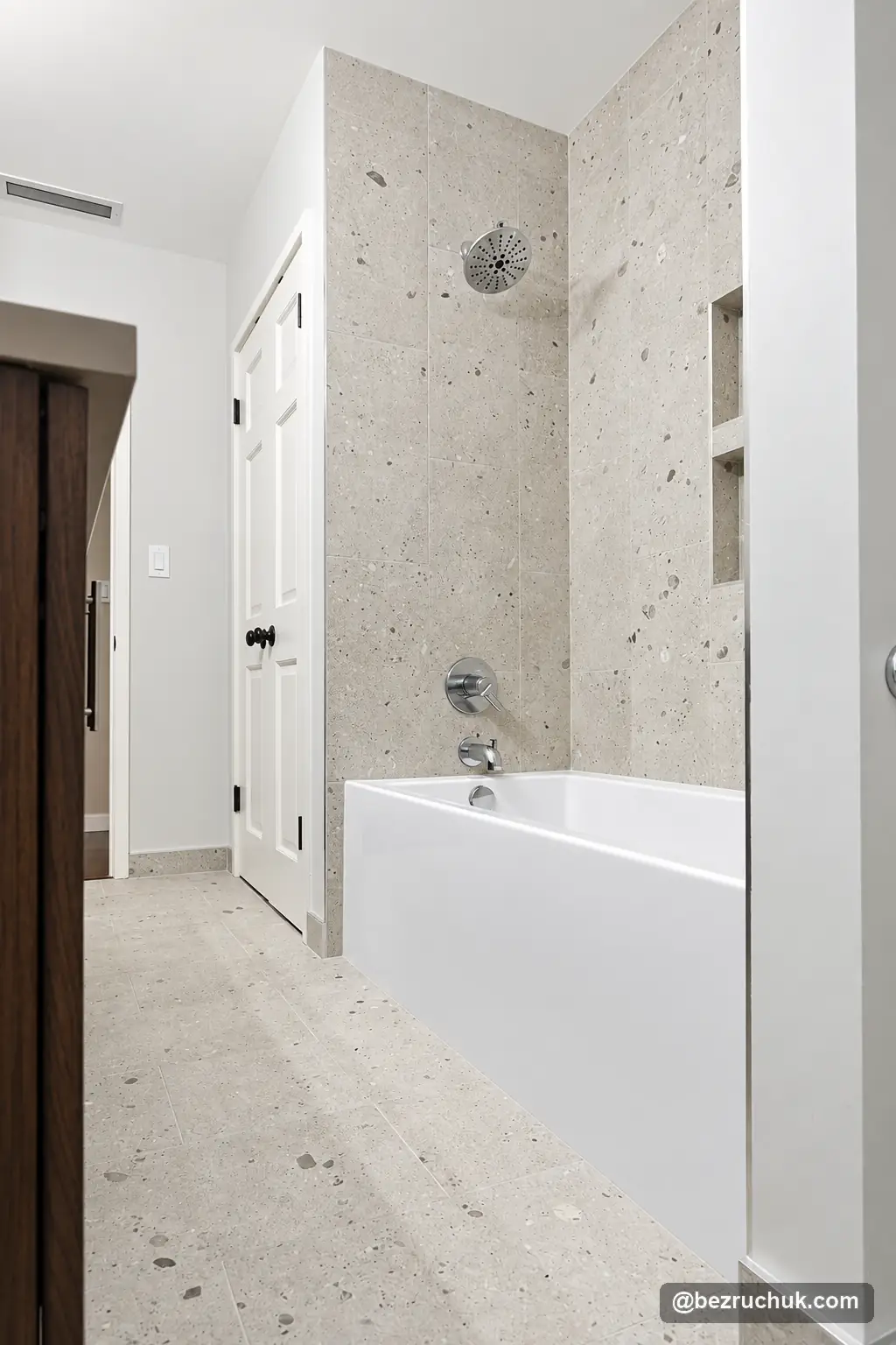 - project image Round chrome shower head and white bathtub surrounded by light speckled tile