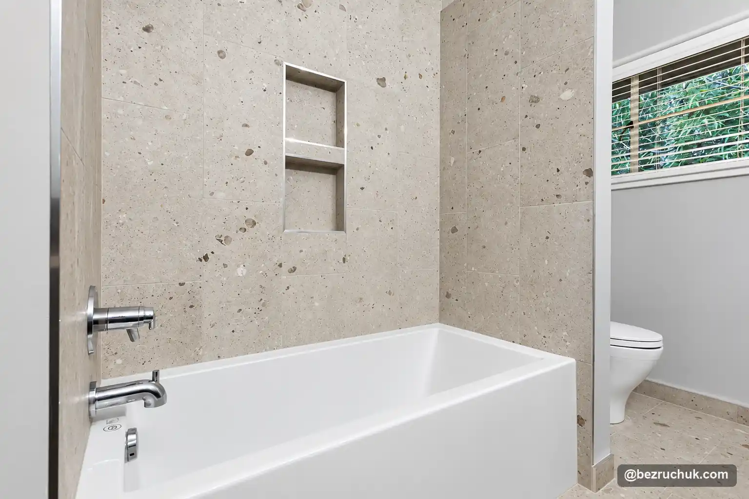 - project image White bathtub with a light speckled tile surround and a two-level recessed niche
