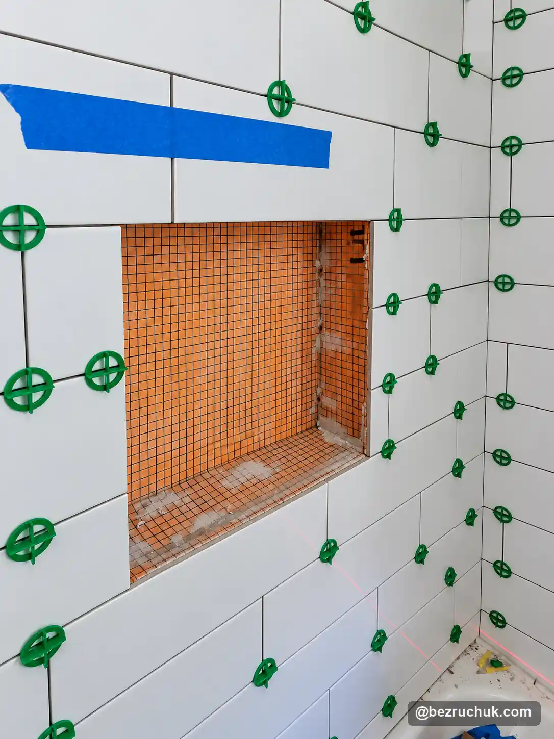 - project image Orange waterproofing material inside a niche during white subway tile installation