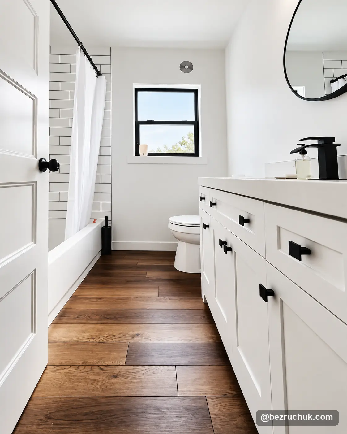 - project image White bathroom vanity with black hardware, round mirror and wood-look flooring