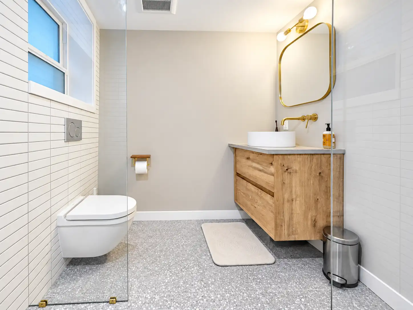 Small bathroom remodel in Seattle with a floating wood vanity, brass accents, white tile and wall-hung toilet