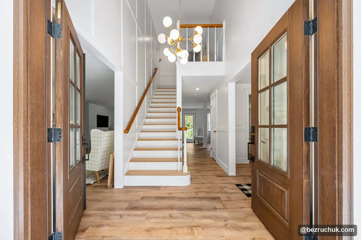 Wide entry view of a board and batten wall, wood stair treads and a globe chandelier
