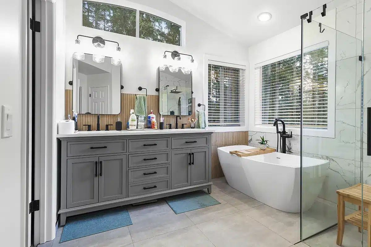 Visit our project page to see this elegant Sammamish bathroom remodel with a dual-sink grey vanity, freestanding bathtub, and glass shower enclosure in Klahanie.