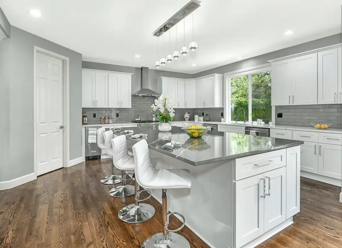 A modern kitchen remodel with white shaker cabinets, gray backsplash, and updated lighting fixtures.