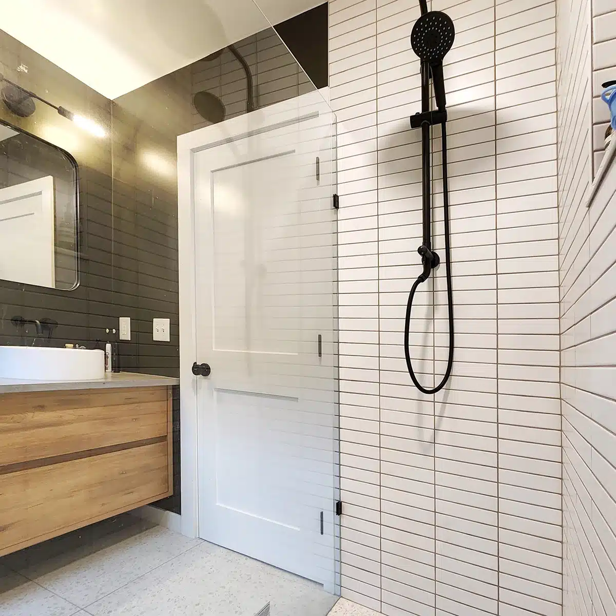 Modern bathroom shower with sleek black showerhead and white subway tile, complemented by a wooden vanity.