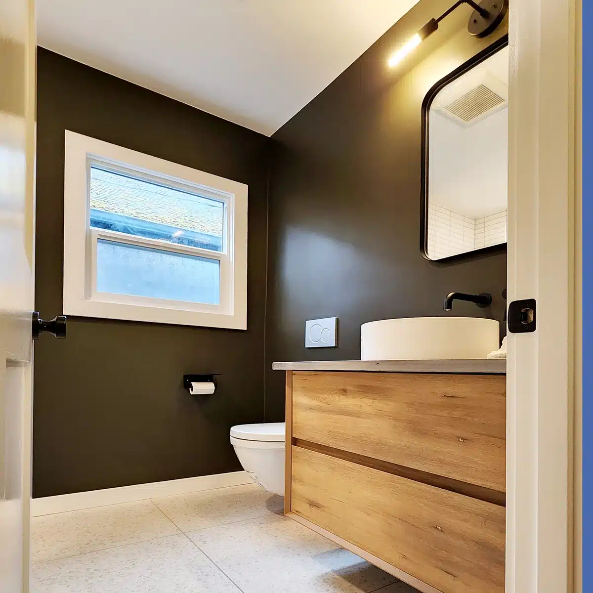 Compact and stylish bathroom design featuring a dark wall, wooden vanity, and wall-mounted toilet.