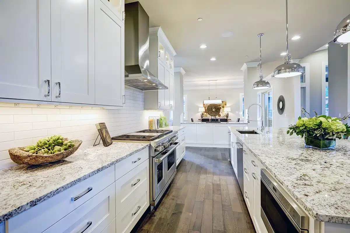 A long, spacious Tacoma kitchen with white shaker cabinets, granite countertops, and a subway tile backsplash, highlighted by natural light.