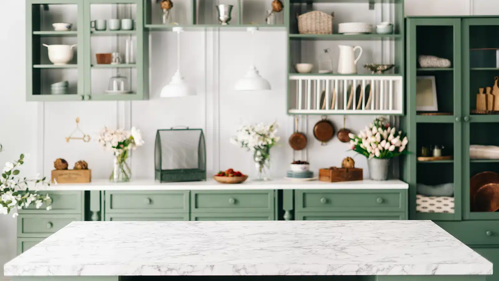 A kitchen with a vintage charm featuring sage green cabinetry, marble countertop, and open shelving filled with kitchenware.