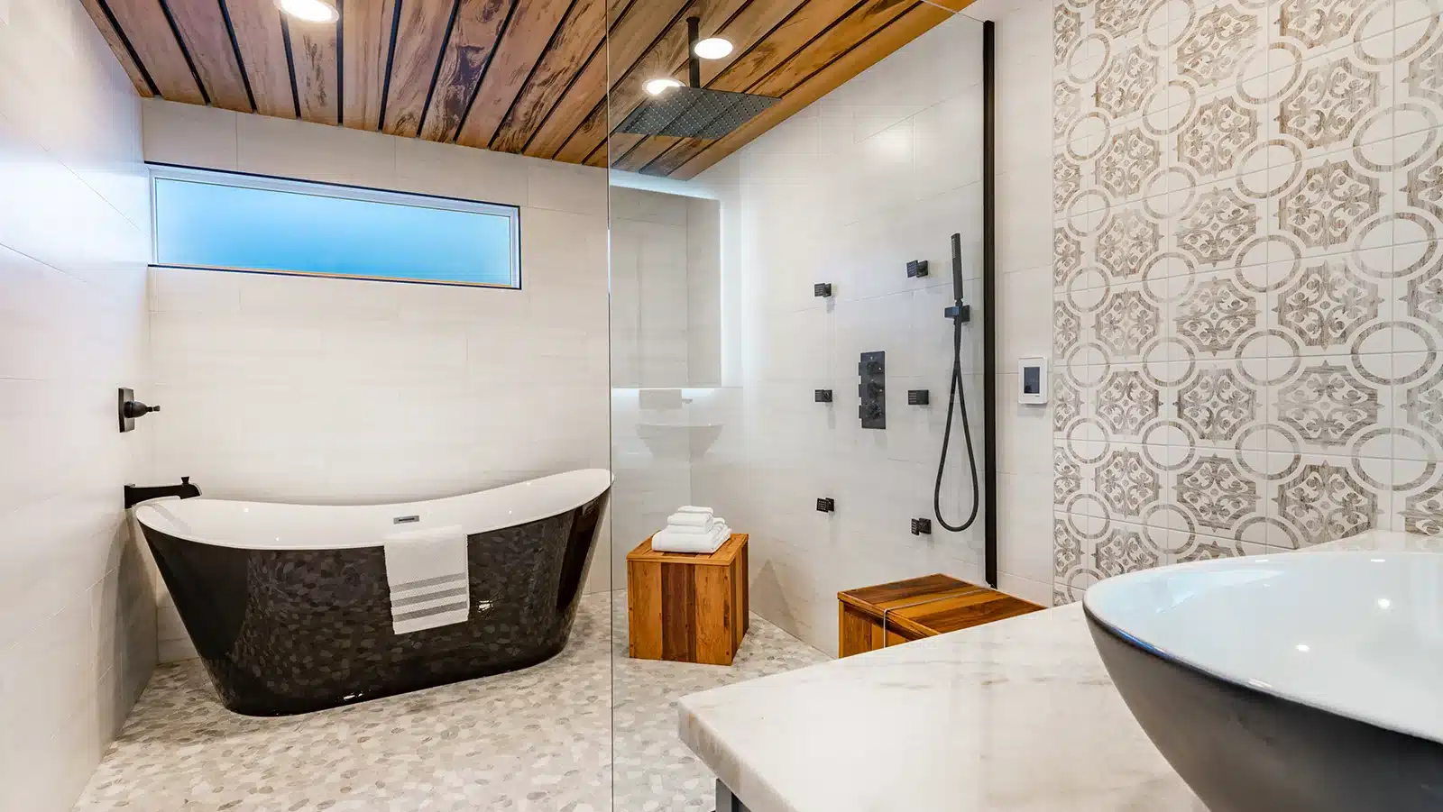 Modern and stylish bathroom with a freestanding black bathtub, tiled walk-in shower, wooden accents, and patterned wall tiles.