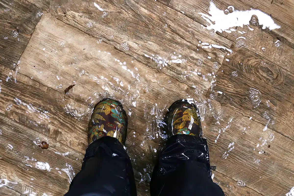 Feet in patterned boots on a waterlogged wooden floor, indicating indoor flooding.