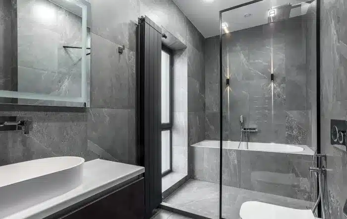 Luxurious dark gray bathroom interior with large mirror, walk-in shower with glass doors, and stylish pendant lights.