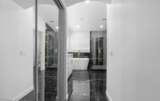- project image Entrance view into a luxury master bathroom with glossy black tile and gold finishes. Featuring modern bathroom renovations.