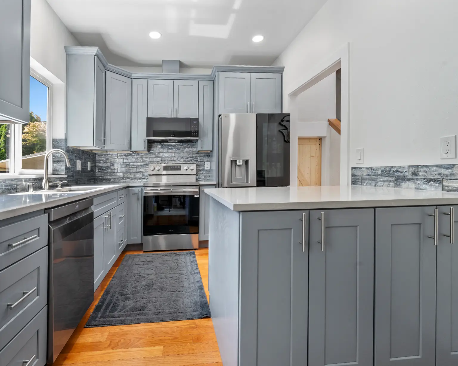 After kitchen remodel in Puyallup with soffit removed, gray shaker cabinets, quartz counters, and glass tile backsplash.