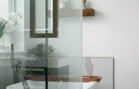 Custom Shower Glass Hardware Detail Close-up of custom glass shower door handle with floating wood shelves and freestanding tub in background.