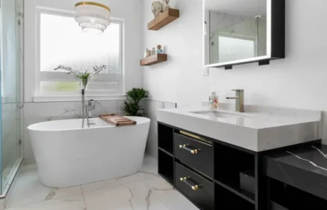 Modern Vanity and Lighting After Bathroom Remodel Modern bathroom with black vanity, integrated mirror lighting, freestanding tub, and marble-look tile flooring.