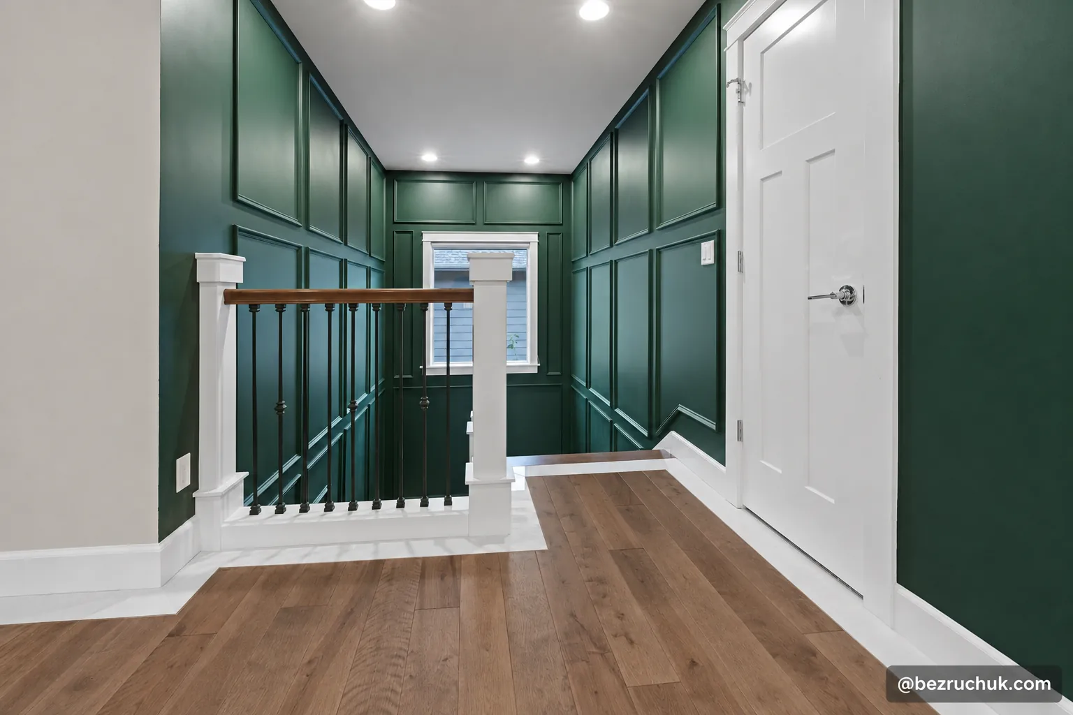 Brown wood landing with a white tile border beside green picture frame molding and a stair railing by bezruchuk inc