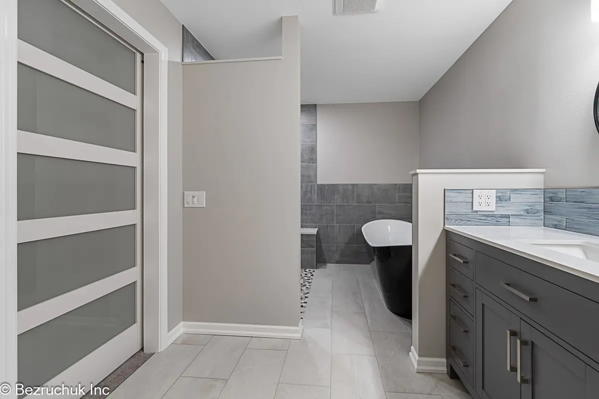 Passage between the bathroom vanity and partition leading to a black-and-white freestanding tub.