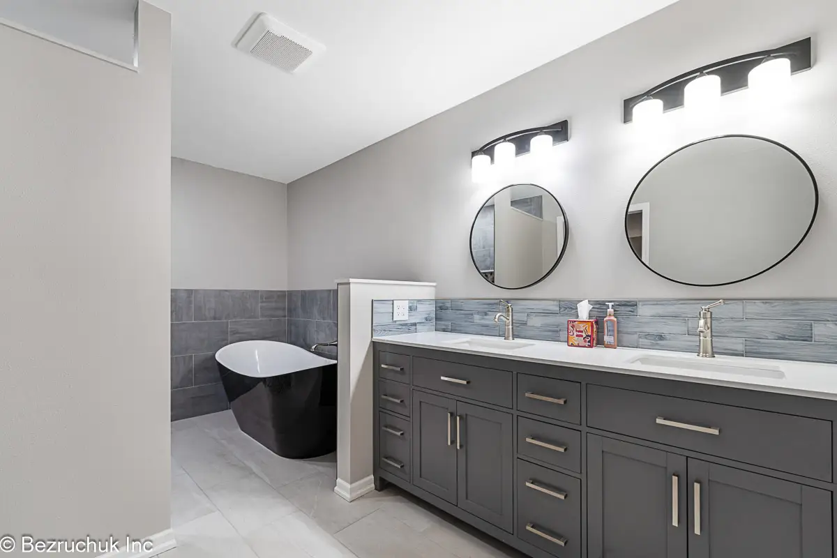 - project image Gray double vanity with two round mirrors and a blue-gray tile backsplash