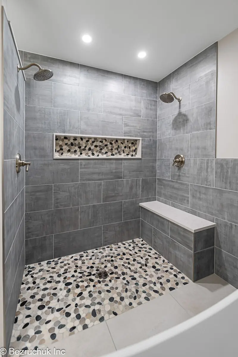 - project image Two wall-mounted showerheads above a pebble mosaic floor and tiled bench