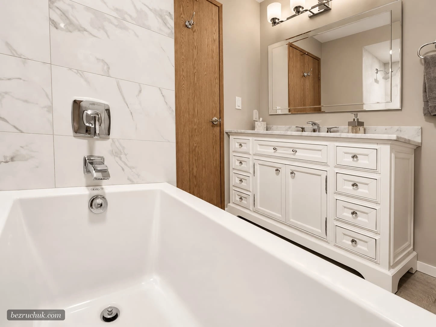 White bathtub beside a classic white vanity and Carrara-look porcelain tile in a renovated Renton condo bathroom