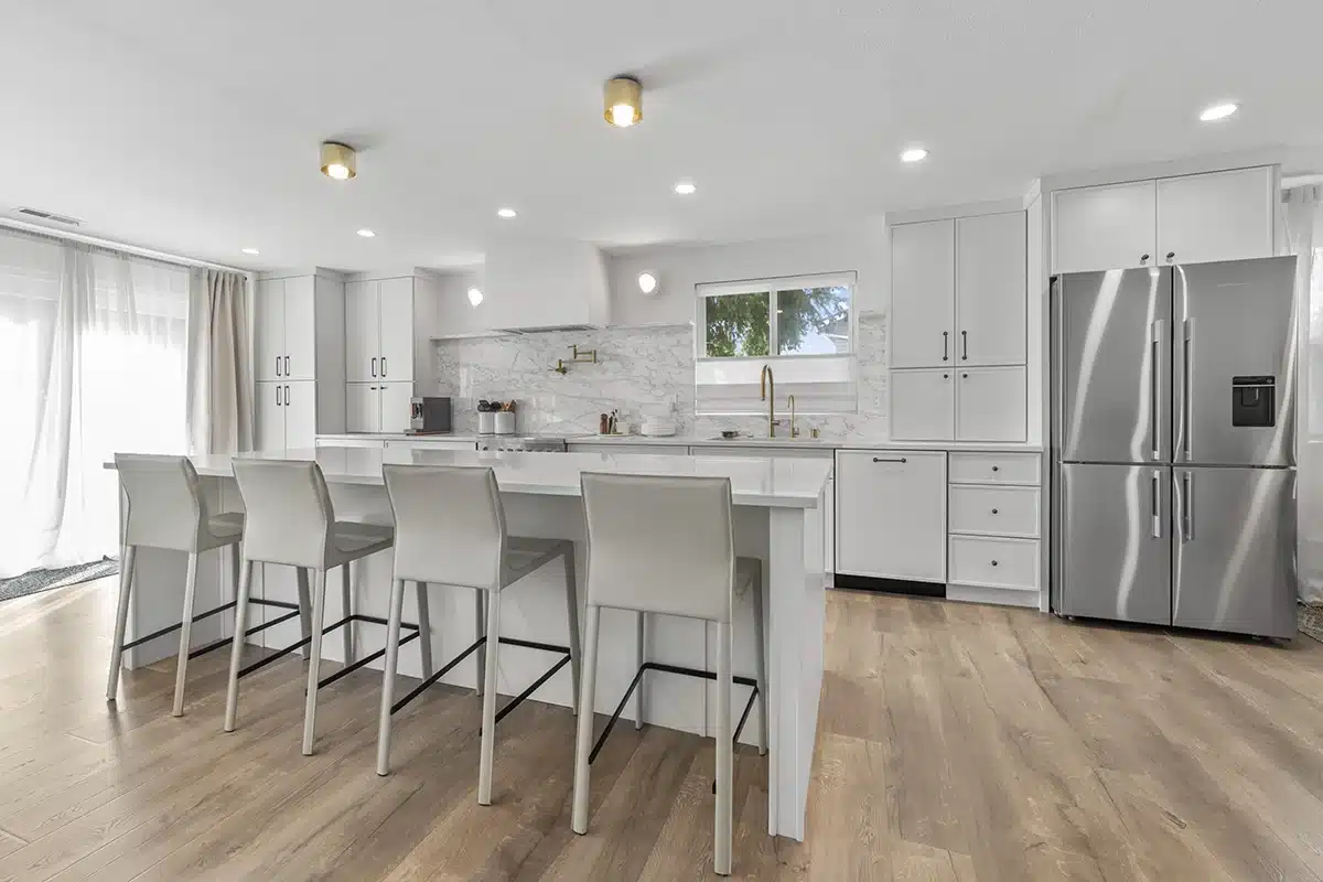 Finished kitchen remodel with white cabinetry, a large white island with seating and wood-look flooring