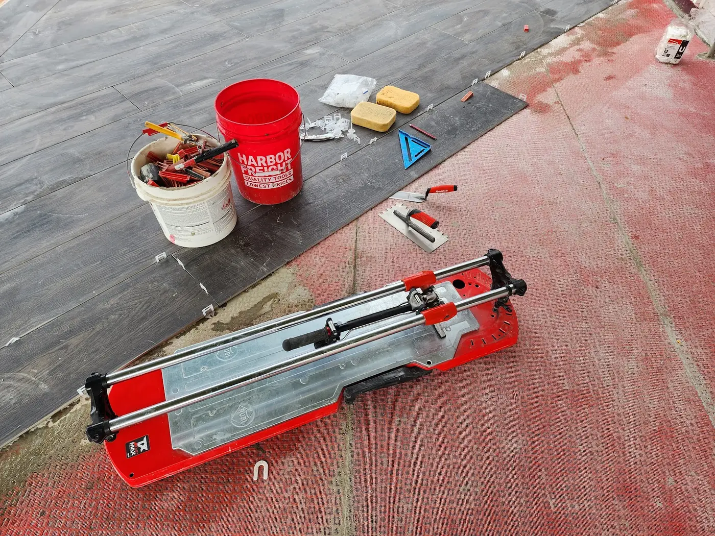 - project image Porcelain planks, a tile cutter and tools beside RedGard Uncoupling Mat during deck installation.