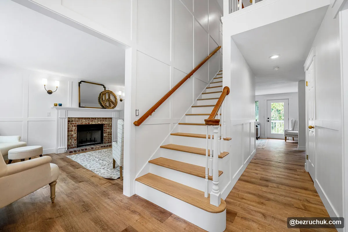 Whole-home renovation with white paneled walls, a staircase with wood treads and a living room with a brick fireplace